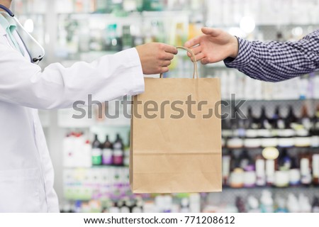Cropped shot of a pharmacist in white labcoat handing shopping bag with purchased medications to his male client pharmacy drugstore health buying consumer customer purchasing retail store. Royalty-Free Stock Photo #771208612