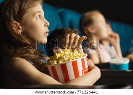 Close up shot of a pretty little girl grabbing popcorn from the bucket while watching a movie at the cinema looking entertained and fascinated copyspace kids lifestyle leisure activity hobby emotions