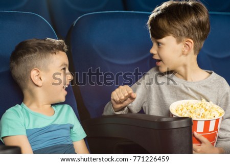 Adorable little boys having fun at the cinema talking and laughing while watching a movie together friendship brothers brotherhood friends children happiness communication interacting