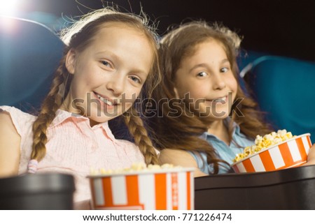 Cheerful young girl smiling at her little brother while watching a movie together at the cinema family kids children childhood siblings positivity enjoyment leisure holidays weekend popcorn 