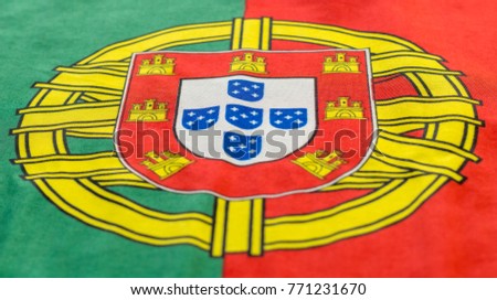 A Portuguese flag is pictured as it lays on a flat surface. The Coat of Arms in between the bold red and green colors is a great symbol for the country of Portugal.