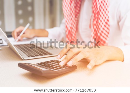 Arab Business man or accountant or banker making calculations. Savings,Business Financing Accounting Banking and economy Concept. ,Image of female hands using calculator on desk about cost on office. Royalty-Free Stock Photo #771269053