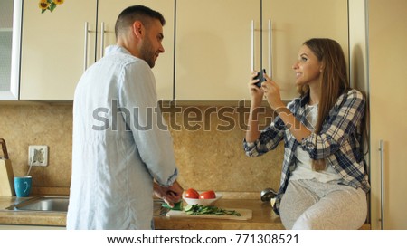 Attractive couple cooking in the kitchen and taking photo using smartphone fo sharing social media at home