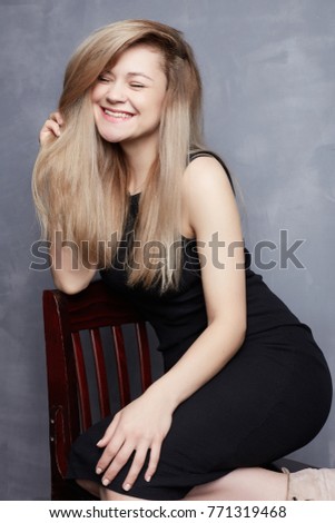 Positive human facial expressions, emotions, reaction, feelings. Vertical studio portrait of happy blond elegant lady with closing eyes, laughing from bottom of heart, posing in gray wall background.
