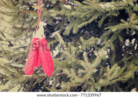 Red mittens with paper dog figure on prickly fir tree green branches. Vintage toned image.