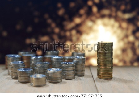 two separate pile of coins on wooden board. business alternative concept. blurred gold light effects in background.