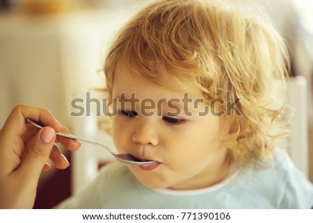 cute fair-haired blond hazel-eyed kid little child baby boy fed with spoon eating photo portrait on blurred background, horizontal picture
