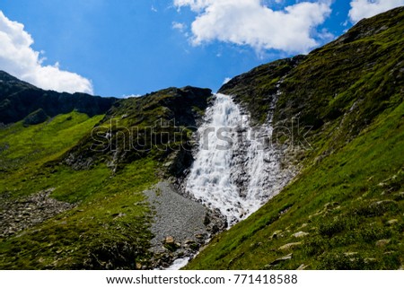 water fall in the austrian alp national park called "fallbach" with green grassland all around and a rock ridge at the top