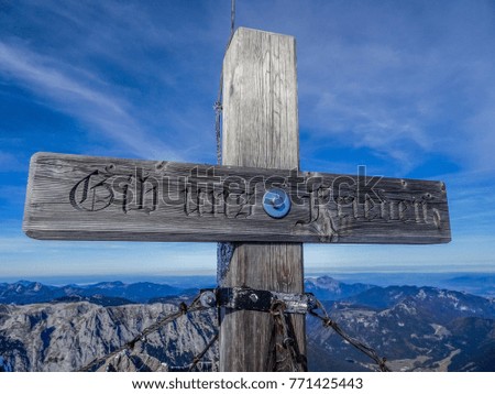 the cross of the bavarian mountain summit "hochkalter" with the words "gib uns frieden" - "give us peace" and a unique landscape behind with a mountain panorama at the horizon and a blue sky