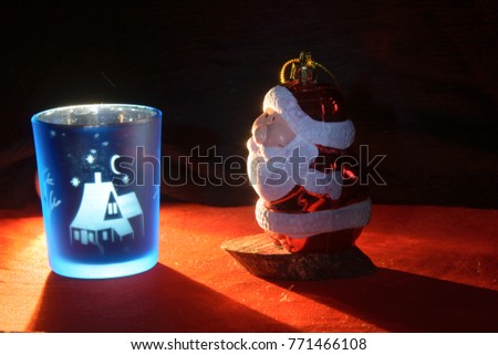 Santa Claus looks at the blue glass with a picture of a winter evening in the village, with a crescent and stars.