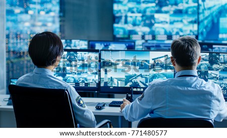 In the Security Control Room Two Officers Monitoring Multiple Screens for Suspicious Activities, They Report any Unauthorised Activities. They Guard Object of National Importance. Royalty-Free Stock Photo #771480577