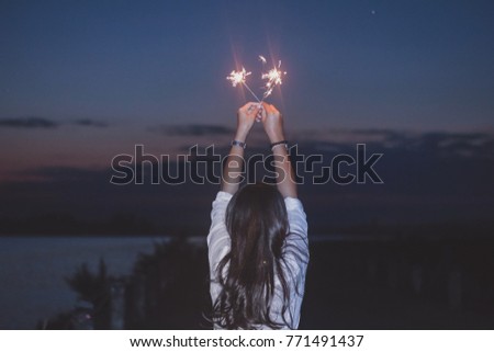 Christmas and new year celebration holiday concept,Blurred woman hand holding bright burning Christmas sparkle on nature landscape and twillight sky background.Winter vintage film grain filter style.
