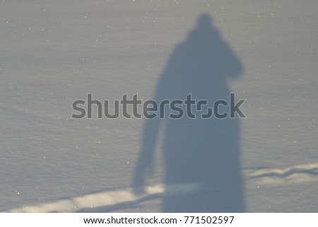 The shadow of a man on white snow, a snowdrift. Large silhouette, winter clothes and mittens, photographer. Winter background