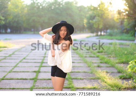 female nature keeps his hat summer sun sunset looks pleased. azitka woman black hair white shirt black shorts dancing around the trees looking at the camera. portrait. spinning