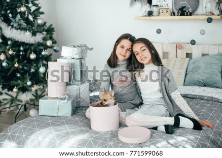 Two beautiful sister girls are sitting on a big bed and looking at the gifts