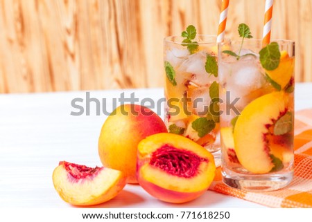 Peach summer cocktail or lemonade with ice and mint leaves. Cold refreshment organic non-alcohol drink with ripe nectarine fruit on wooden background.
