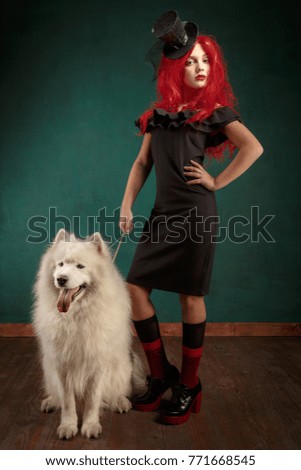 Winter dog holiday and Christmas. Girl in a black dress and with red hair with a pet in the studio. Christmas woman with a beautiful face and pet.