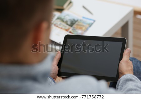 Male hand holds tablet pad in home setting while sitting on the couch engaged an internet surfing using application to press a finger on the display leisure listering music concept closeup. Royalty-Free Stock Photo #771756772