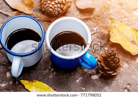 Blue and white cups of coffee on ground, pine cones with leaves beside mugs, sunlight shining on a part, warm tone photo