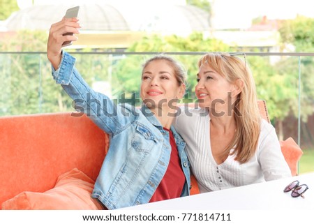 Mature woman and her daughter taking selfie in cafe