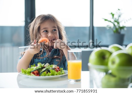 Portrait of cheerful asian girl eating salad with joy. She is looking aside with curiosity and smiling Royalty-Free Stock Photo #771855931