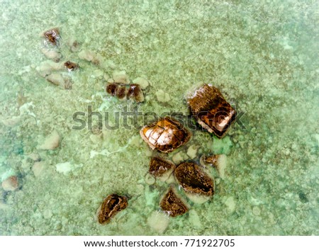 View from above of rocky reefs partially submerged in a blur view of shallow clear turquoise sea