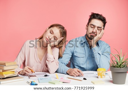 Portrait tired crew of office workers sit at table, fall asleep after working long hours on preparing startup project, feel tiredness, isolated over pink background. People and overworking concept Royalty-Free Stock Photo #771925999