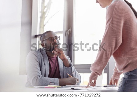 Indoor shot of serious black male boss looks attentively at unrecognizable female secretary, litens to her presentation and predictions about future sales, analyze current situation together