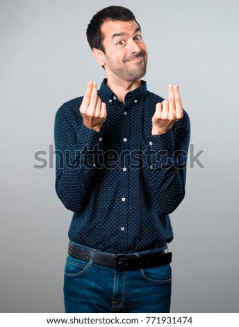 Handsome man making money gesture on grey background