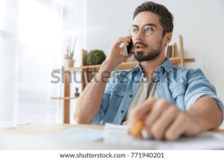 Serious concentrated fashionable male office worker calls to colleague on cellular, has phone talk, try to arrange meeting discuss everything alive. Creative male designer shares idea with companion Royalty-Free Stock Photo #771940201