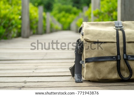 The brown camera bag on wooden bridge to forest for travel trip with adventure lifestyle in holiday.