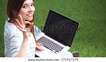 Young woman with laptop sitting on green grass 