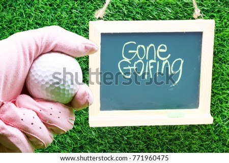 Hand is holding golf ball double exposure with gone golfing sign on chalk board