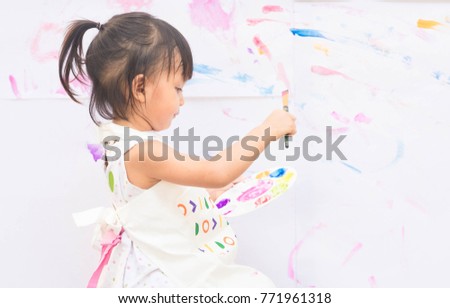 Cute asian little girl is sitting and  holding the brush and color palette for painting the color to the white paper, concept of art and education for kid.