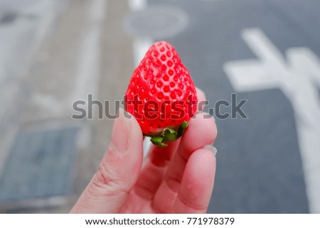 Selective focus of red strawberry on woman hand with blurred of street background