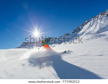 Young skier running downhill in beautiful Alpine landscape. Fresh powder snow, blue sky on background. Winter sports and outdoor activities