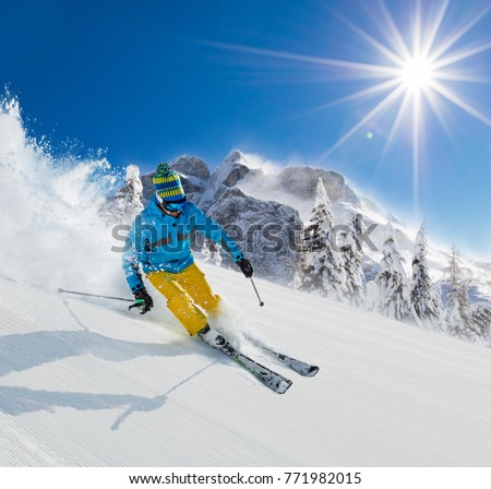 Skier on piste running downhill in beautiful Alpine landscape. Blue sky on background. Winter sports and outdoor activities