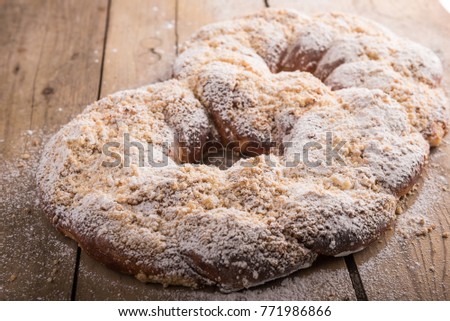 Big sweet kringle with butter crumbs and powdered sugar on wood table. A homemade dessert with a tasty and heartwarming look.