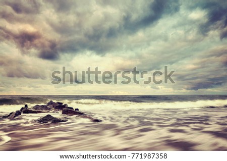 Vintage toned picture of a beach with stormy sky, motion blurred water.