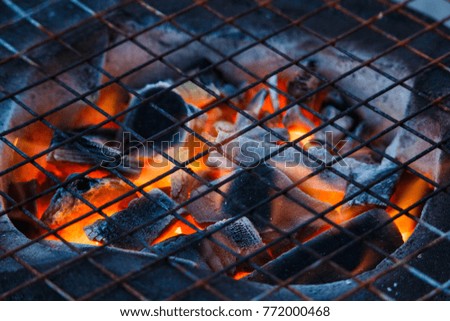 Close up of a burning hot fire in a portable barbecue with an empty grill and a wicker picnic hamper visible.