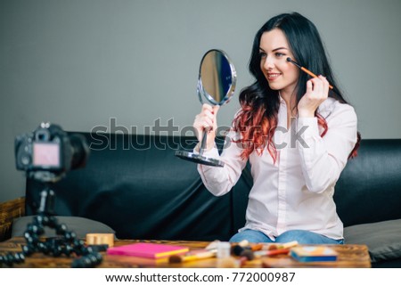 Young female blogger with makeup cosmetics recording video at home
