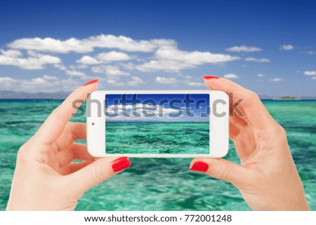 female hand holds a mobile phone and take pictures of a beautiful beach on a caribbean in summer time with not focus background 