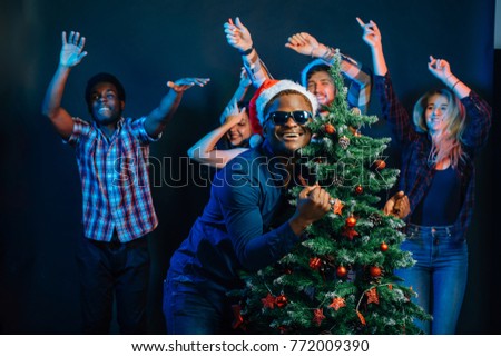 african american man hugging with cristmas tree and people dancing at background on new year party