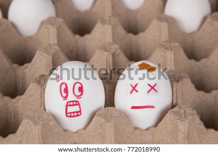 concept. two eggs among the rest in the package. an egg with a smile of horror looks at the broken egg