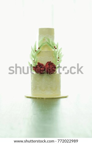 Three tier wedding cakes with red flowers and laurel wreath leaves