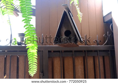 Small wood bird’s house is hanging above iron fence with blurry green leaf on wooden background. It’s not the cage. Concept be used for freedom life can select to use it. Blur picture.
