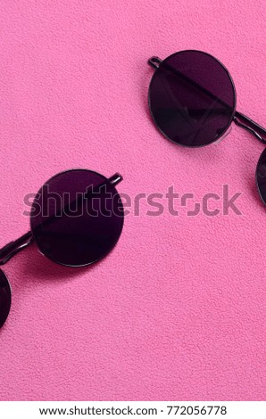 Two stylish black sunglasses with round glasses lies on a blanket made of soft and fluffy light pink fleece fabric. Fashionable background picture in female colors