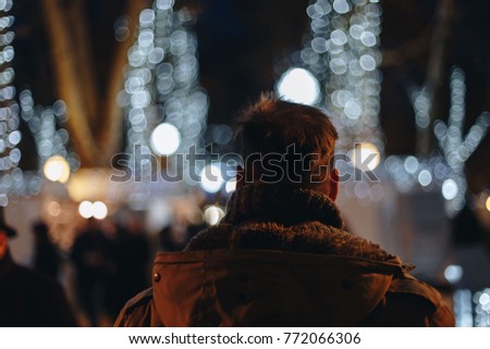 silhouette of a man, alone in christmas illumination light in winter park. back view of a traveler visiting a european xmas market.

