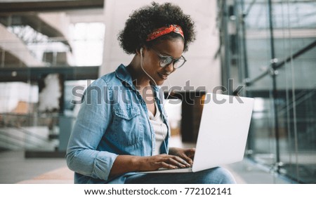 Smiling young African female university student sitting on a campus bench working on a laptop while preparing for an exam