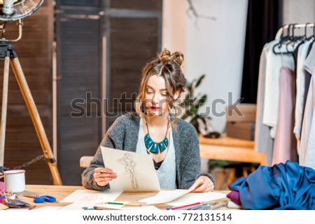 Young female fashion designer sketching drawings of the clothes sitting at the beautiful office with different tailoring tools